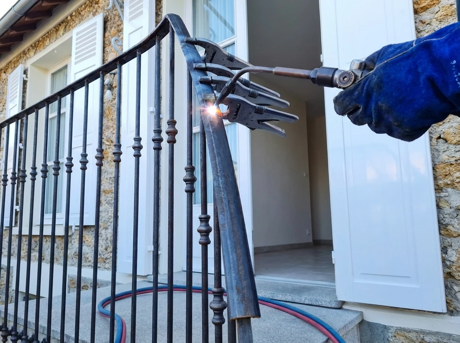 Scène extérieure montrant un artisan travaillant le métal sur une enclume, tenant un marteau et un ciseau à froid