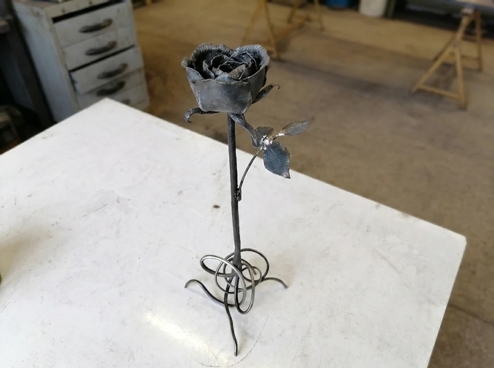Vue en gros plan d'un soudeur professionnel protégé par un masque en uniforme travaillant sur la sculpture en métal à la table de l'atelier de tissu industriel devant quelques autres ouvriers